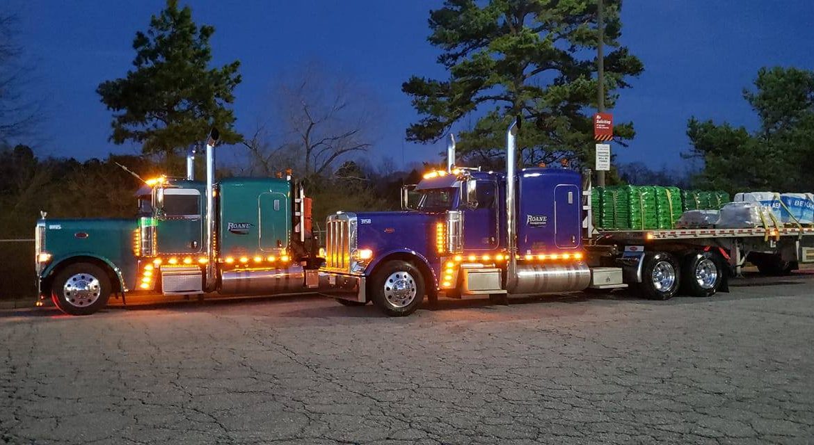 Two semi trucks hauling flatbeds sitting at a truck stop